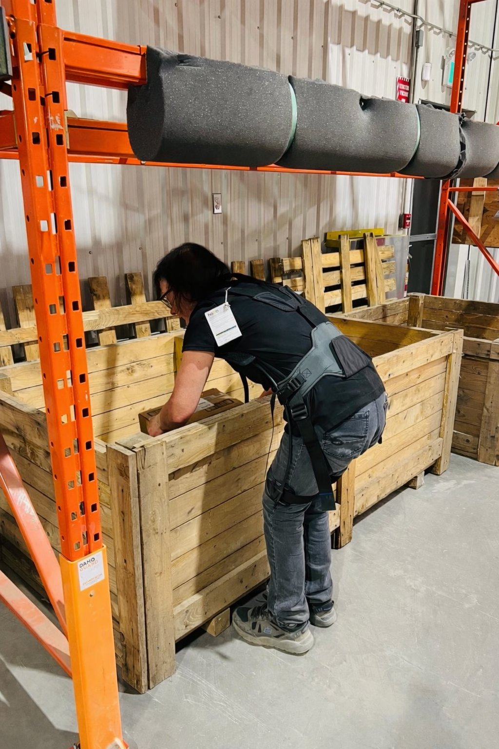 Worker leaning into a deep wooden shipping crate wearing a Hapo Back exoskeleton to protect the lower back
