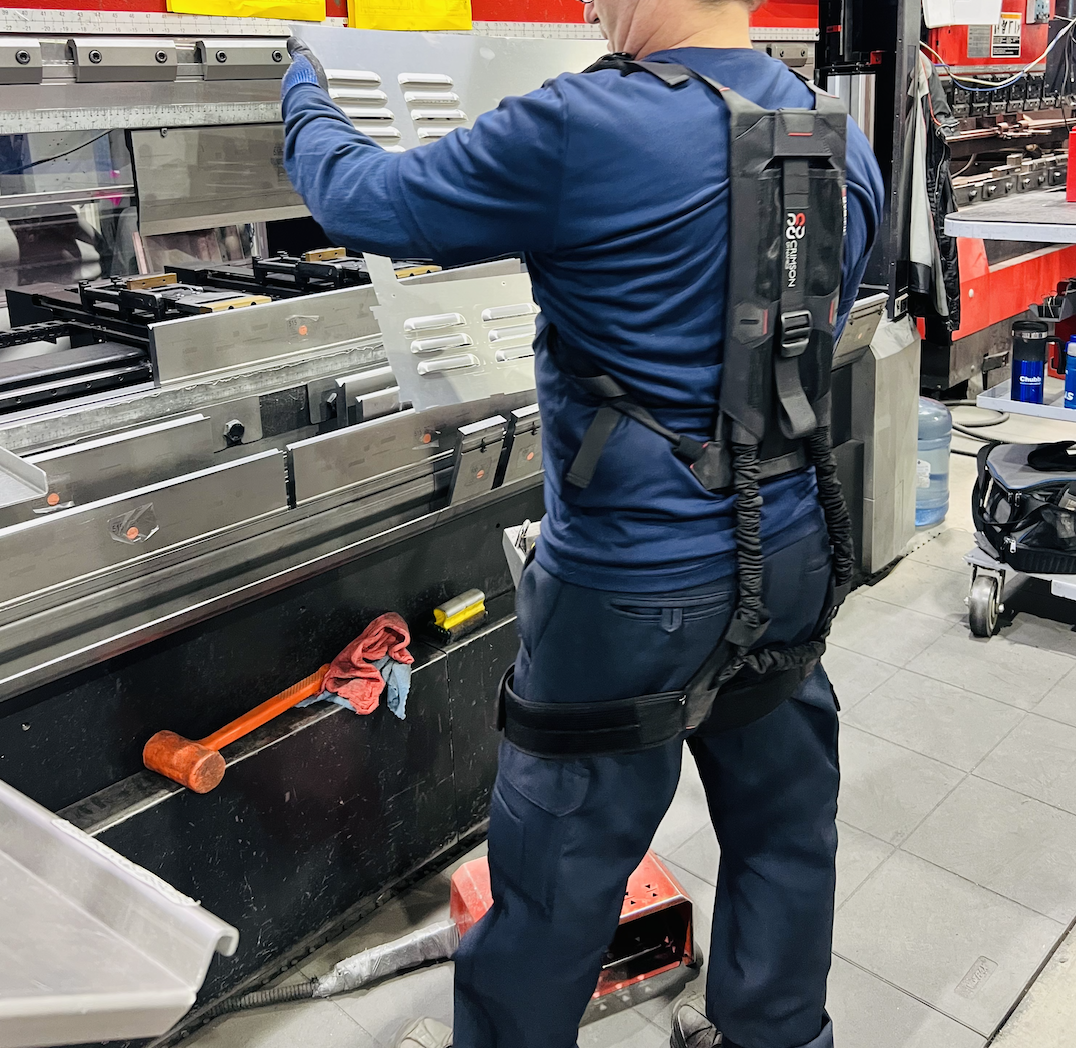 Worker wearing a Crimson Fit exoskeleton at a metal press brake in a fabrication environment