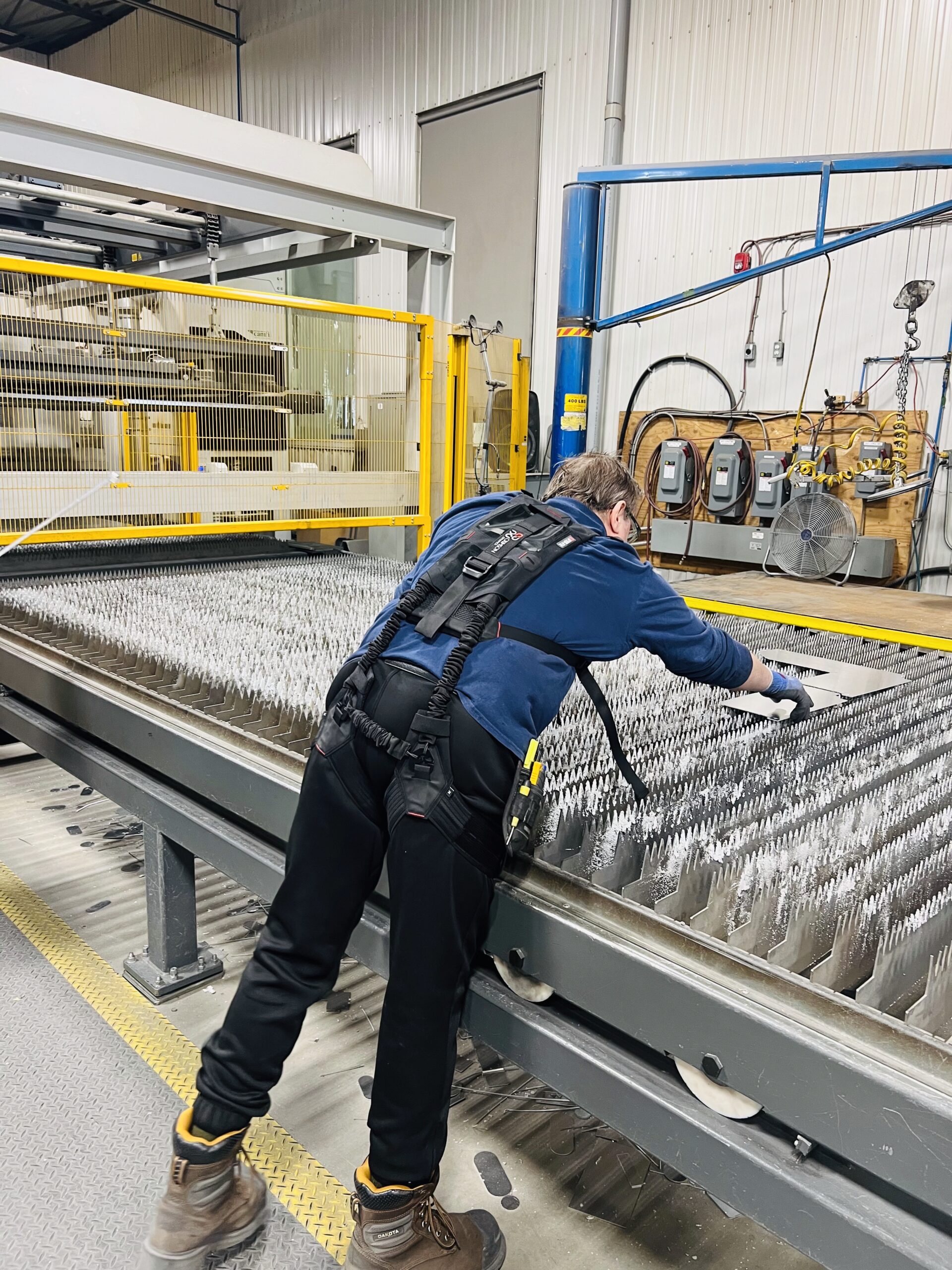 Worker at a laser cutting station wearing a Crimson Fit exoskeleton in a Canadian metal fabrication plant